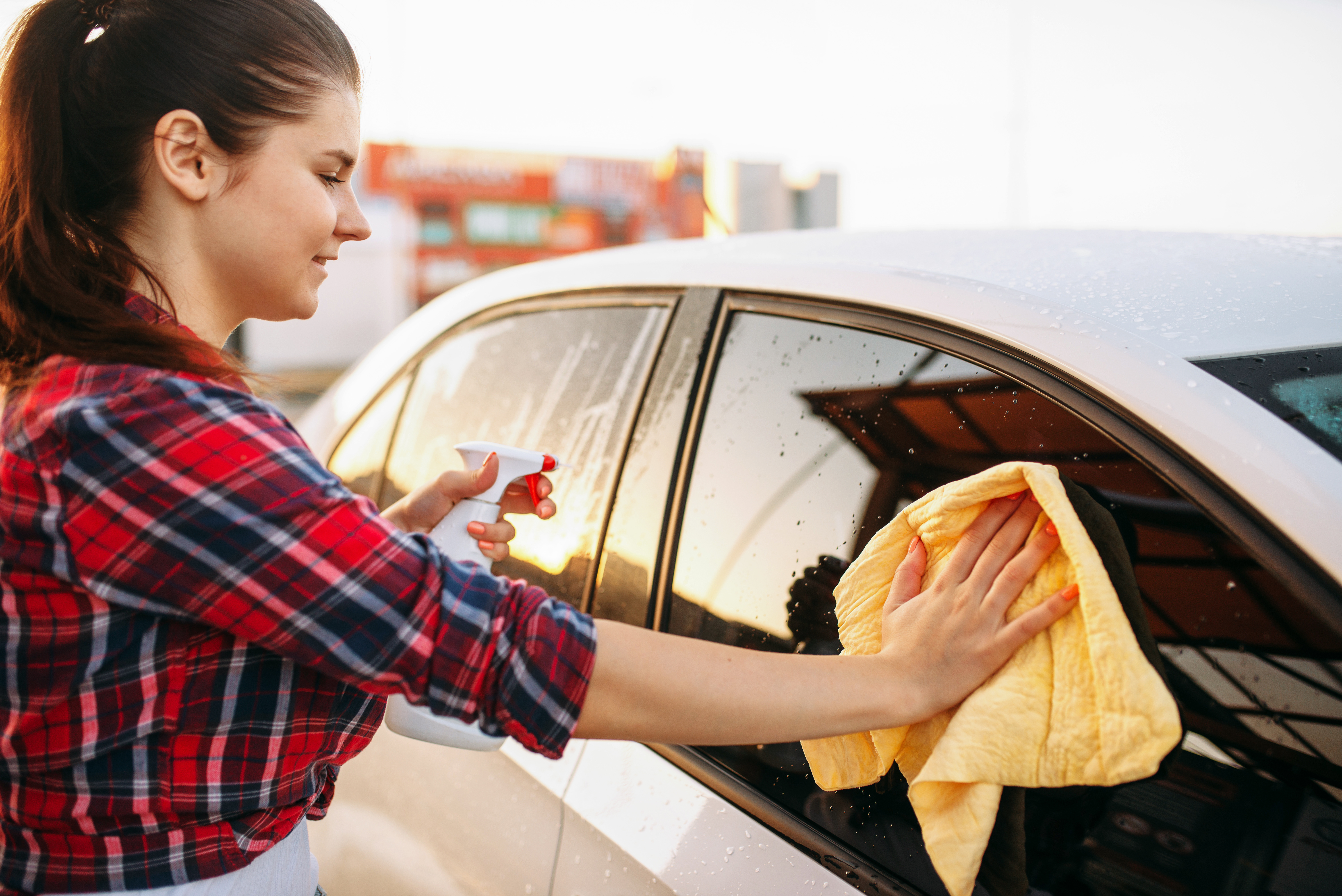 Woman cleans front glass of the car with spray - Best Shine Car Wash